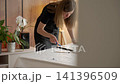 Female artist creating a textured picture on canvas, applying white plaster paste with a blue palette knife at table. Concept of handmade painting and creative hobby 141396509