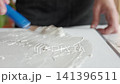 Hand applies white textured paste on canvas with a small spatula, creating a relief surface. Concept of DIY textured art and handmade wall decor. 141396511