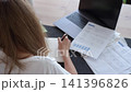Woman checking paper bills at laptop and writing notes in notebook. Concept of household budget, paying bills and tracking expenses 141396826