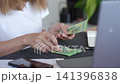 Woman counting euro cash at a table with laptop, phone and papers while planning household expenses. Concept of personal finance and budget planning. 141396838