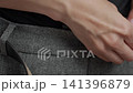 Woman fastening button on gray trousers while getting dressed in wardrobe, close-up. Concept of outfit detail and morning routine 141396879