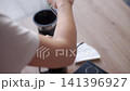 Hands grind coffee with a manual grinder near a pour over dripper on a wooden table. Concept of coffee preparation, fresh grinding and manual brewing. 141396927