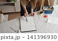 Female artist shapes relief texture on canvas with white plaster paste and palette knife at a covered work table. Concept of DIY wall decor and creative hobby. 141396930