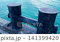 Weathered mooring bollard on a wooden dock with rippling blue water 141399420