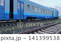 Blue passenger train moving away on railway tracks with freight cars in background under twilight cloudy sky, concept of travel and transportation 141399538