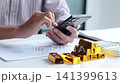 Businessman checking digital gold trading application on smart phone with physical gold bars on the table. 141399613