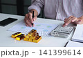 Close-up hands using calculator for gold bar trading analysis. Concept for wealth management, asset protection, and financial planning. 141399614