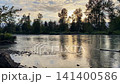 Scenic sunset over a wide river with golden sky reflections and silhouettes of forest trees 141400586