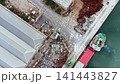 Large amounts of scrap metal are piled up next to a dock with a ship loading cargo at a port during the daytime 141443827