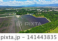Solar panels cover a large field in a rural area surrounded by trees and mountains on a sunny day 141443835