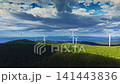 Wind turbines stand on hills under a cloudy sky with mountains in the distance in this landscape taken during the day 141443836