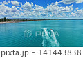 Watercraft navigate clear blue waters near a beach under a cloudy sky during daytime in a sunny location, showing the horizon and shoreline 141443838