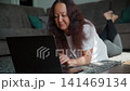 Woman using laptop on floor while relaxing on couch in living room 141469134