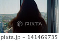 Woman gazing out high rise window at cityscape 141469735