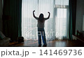 Woman celebrating victory arms raised high rise apartment window cityscape view 141469736
