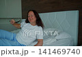 Woman stretching arms up on bed in bright morning light 141469740