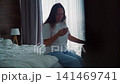Woman checking phone while sitting on bed with luggage, hotel room with city view 141469741