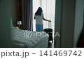Woman with luggage standing by window in hotel room 141469742