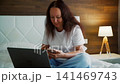 Woman Working on Laptop in Bedroom with Warm Lighting 141469743