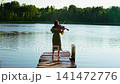 Young woman playing violin on rustic wooden dock over tranquil forest lake, barefoot musician 141472776