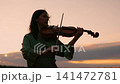 Silhouette of a young woman playing violin outdoors at tranquil sunset, creating peaceful music 141472781