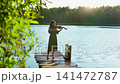 Young woman playing violin on rustic wooden pier beside tranquil forest lake at golden hour 141472787