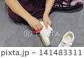 Hands clean a white shoe in a close view with a red sponge on gray floor tiles. 141483311