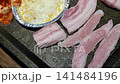 Sizzling Korean BBQ Pork Belly (Samgyeopsal) Grilling with Kimchi and Garlic on a Hot Plate 141484196