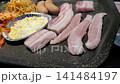 Sizzling Korean BBQ Pork Belly (Samgyeopsal) Grilling with Kimchi and Garlic on a Hot Plate 141484197