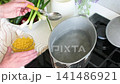 A woman prepares gluten-free pasta in her kitchen using water and a pot. She cooks the pasta while gathering fresh vegetables from her table for a complete meal 141486921