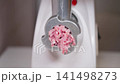 Meat grinding scene. Close view of meat extruding from electric grinder with textured pork. Detailed image showing raw minced pork emerging from meat grinder against white surface 141498273