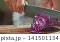 Woman hand slicing purple cabbage with kitchen knife on wooden cutting board 141501134