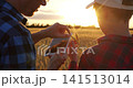 Farmer father and son exploring nature with tablet in golden wheat field during sunset. They engage in learning about agriculture and technology, capturing precious moments full of joy and discovery. 141513014