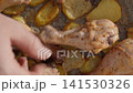 Person checking cooked chicken drumsticks and roasted potatoes 141530326