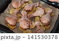 Raw chicken legs on sliced potatoes ready for the oven 141530378
