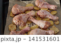 Raw chicken drumsticks and potatoes on a baking tray for roasting 141531601