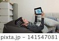 一位女士躺在沙發上，用平板電腦瀏覽投資相關的網站。 141547081