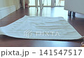 Woman places her bare feet on a white towel on a wooden floor, illustrating the movement and connection between the towel and her feet in a well-lit room 141547517
