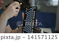 Close-up shot of person hands using handheld air duster to blow dust from blue switches of custom mechanical keyboard. Concept of detailed maintenance and care of computer hardware 141571125