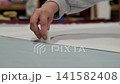 Hands gently place small white object on flat surface. Fingers carefully position item with precision. Soft lighting highlights delicate action. Background blurred, focusing on task at hand 141582408