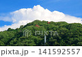 A summer scene of a rural mountain village with towering cumulonimbus clouds; a natural landscape of blue sky and lush greenery. 141592557