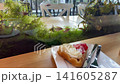 Belgian waffle with whipped cream and fresh strawberries served on a wooden table next to built-in aquarium. Fish swim among green aquatic moss creating a relaxing atmosphere inside a modern cafe 141605287
