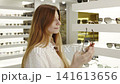 Beautiful woman examines glasses in retail store. Fashionable woman evaluates various eyeglass styles during shopping experience inside an optic store 141613656