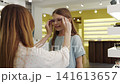 Mother helping her daughter choosing glasses in an optic store. Vibrant eyewear store featuring mother and daughter choosing glasses 141613657