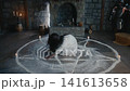 Mad woman reaching forward through chalk pentagram circle under candlelight. Raw expression, long dark hair, torn white dress, wooden floor 141613658