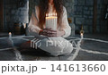 Crop of woman seated on pentagram holding candles, soft halo of light framing focused face and long hair against stone hearth white robe. Mysterious atmosphere, slow breath and drifting 141613660