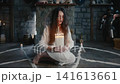 Woman seated on pentagram holding candles, soft halo of light framing focused face and long hair against stone hearth white robe. Mysterious atmosphere, slow breath and drifting 141613661