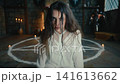 Occult exorcism ritual woman kneeling inside pentagram circle surrounded by candles. Focused gesture performing summoning, antique fireplace backdrop, salt 141613662