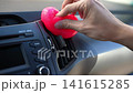 Man cleaning car air vent and dashboard with pink cleaning gel. Close-up of hand using sticky slime to remove dust from vehicle interior. Car detailing and maintenance concept. 141615285