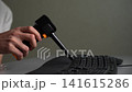 Professional technician using cordless electric air duster to blow dust and debris from between keys of black computer keyboard, ensuring proper electronic maintenance and office hygiene, slow motion. 141615286